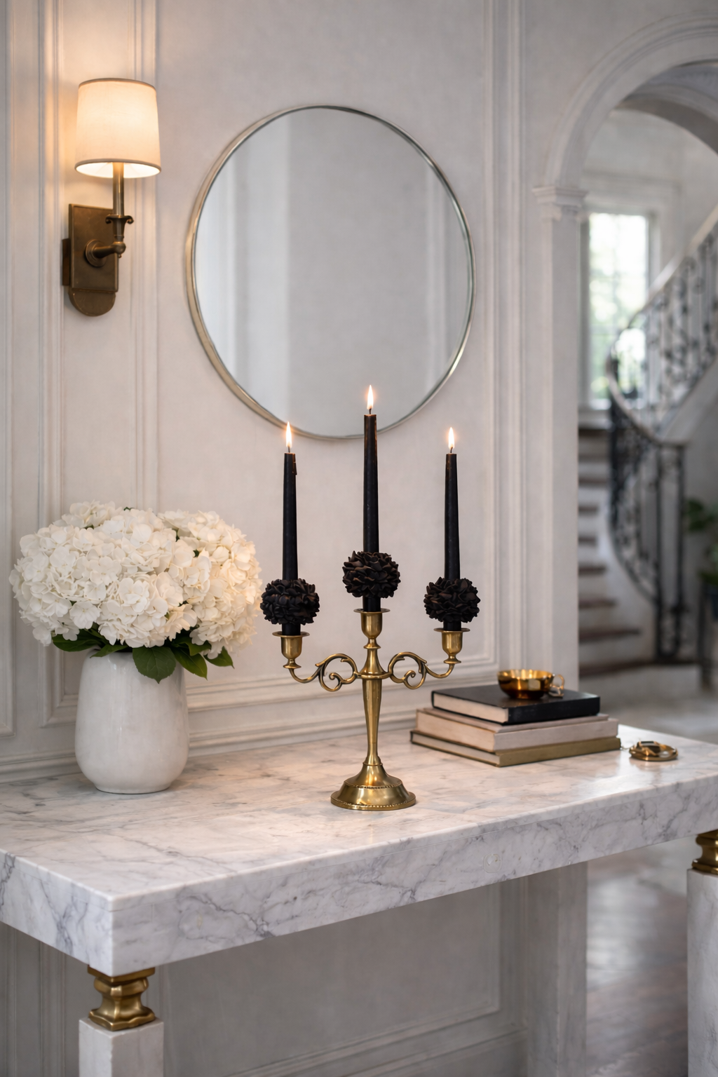 A brass candelabra holding three black TableBlooms tapers on a marble console table beside white hydrangeas